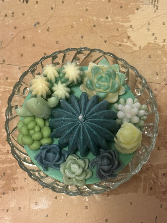 Decorative arrangement of green and blue succulent-shaped candles in a glass bowl.